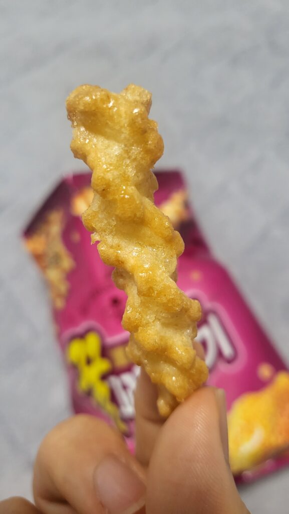 There's a honey twist snack in the background and a hand holding a honey twist snack on top of it